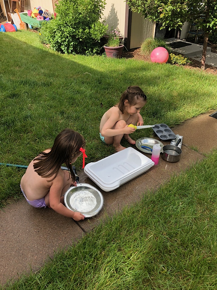 2 girls cleaning up their mud kitchen outside.