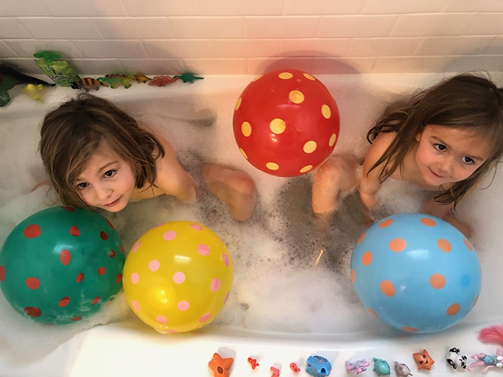 2 girls in a bath tub with balloons.