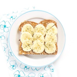 Almond Butter toast with bananas and hemp sprinkles sitting on a round plate.