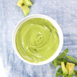 White bowl filled with a green oat baby food puree with produce scattered next to it.