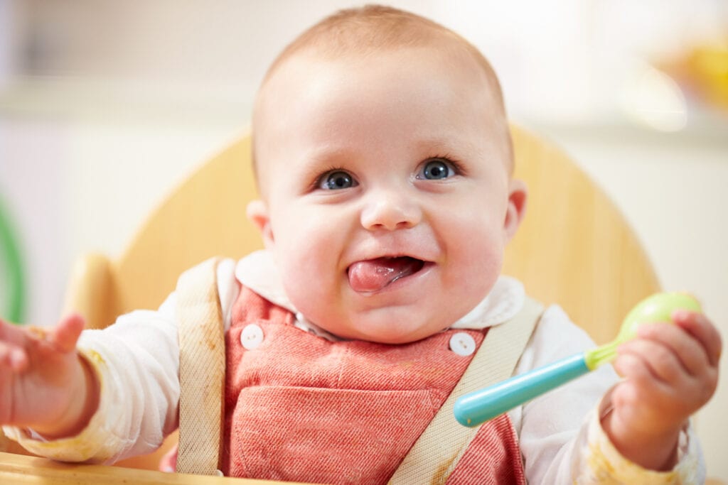 Baby girl in a high chair holding a spoon. 
