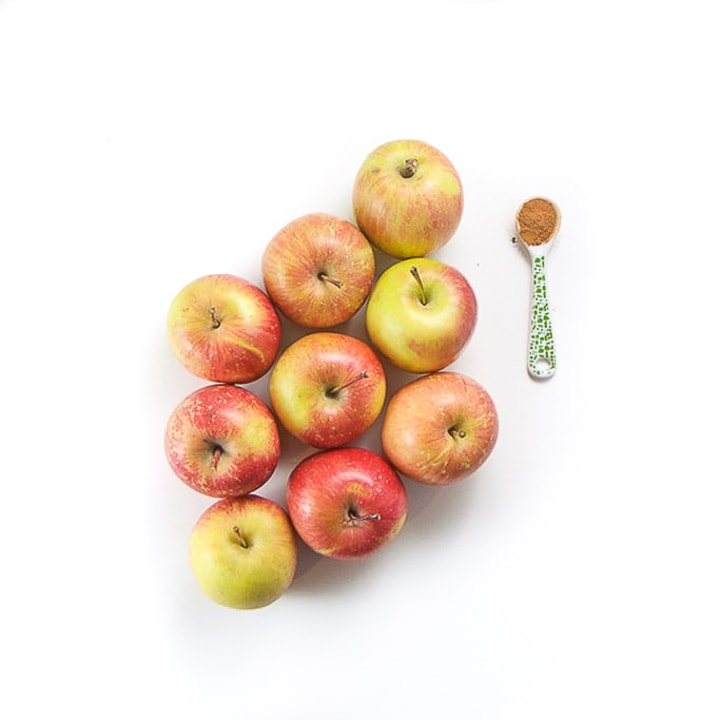 apples on a white surface with a green spoon with cinnamon next to it.
