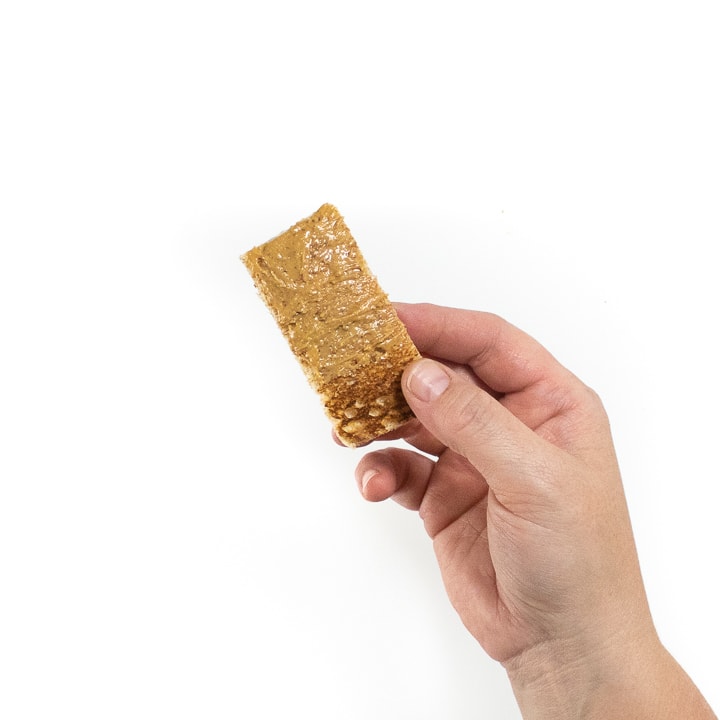Hand holding a piece of toast with nut butter on it.