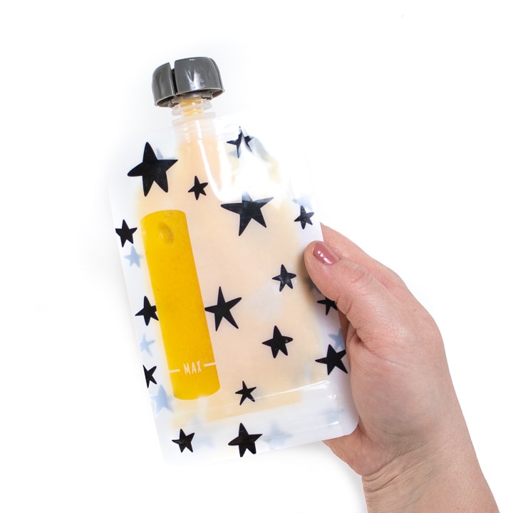 Hand holding a baby food pouch full of peach baby puree.