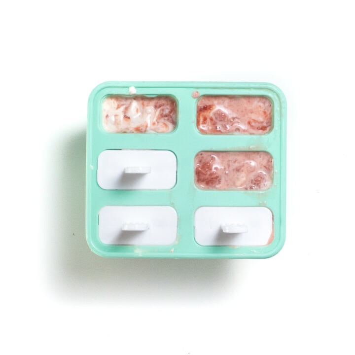 Teal popsicle tray filled with strawberry and yogurt filling for Popsicles.