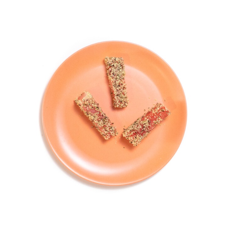 A peach baby plate with three sticks of watermelon world and hemp seeds.