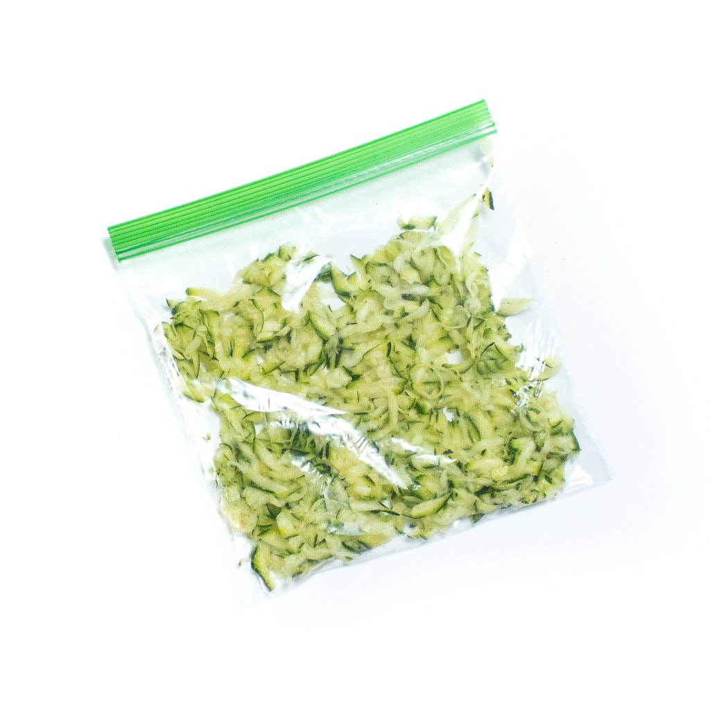 A freezer bag full of grated zucchini against a white background.